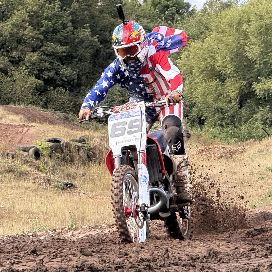 Rider in stars and stripes kit on a red and white bike, roosting out of a turn