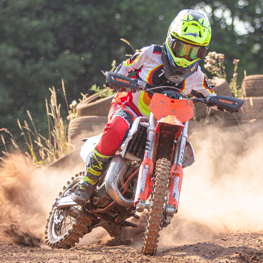Youth rider cornering hard on an orange bike, kicking up sand